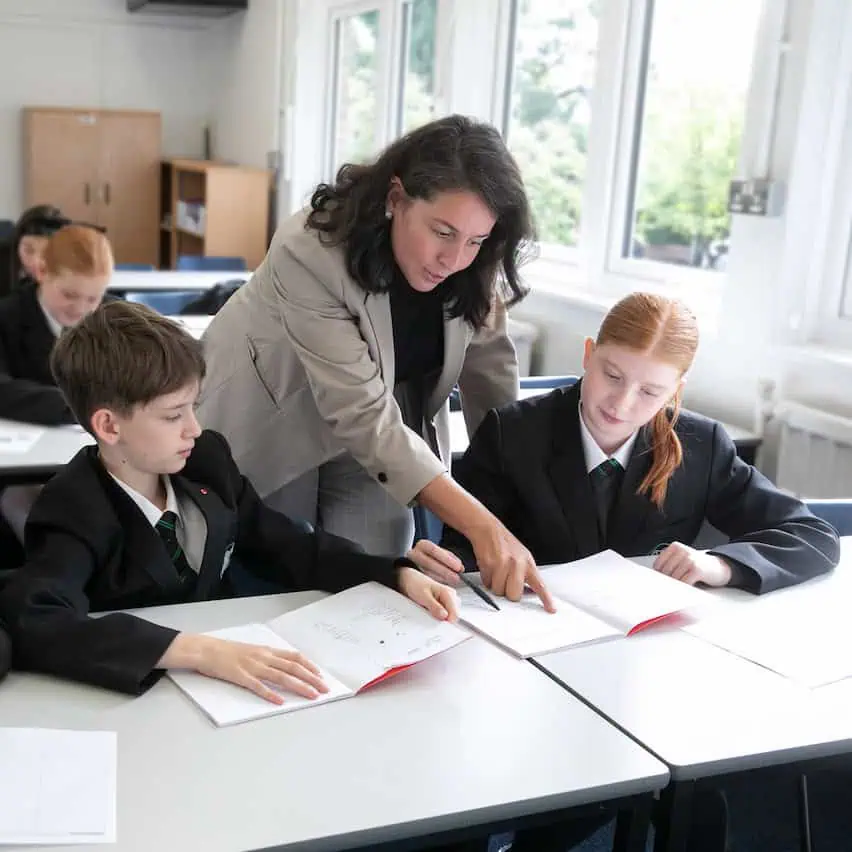 A teacher from Priestnall School guides two students with their work during a lesson.